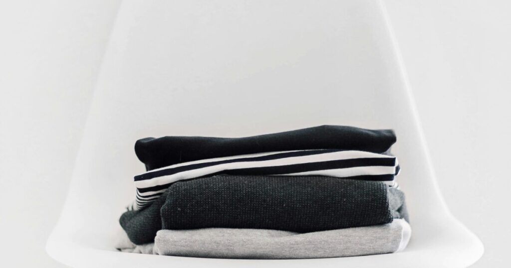 白い椅子の上に積まれたモノトーンの服